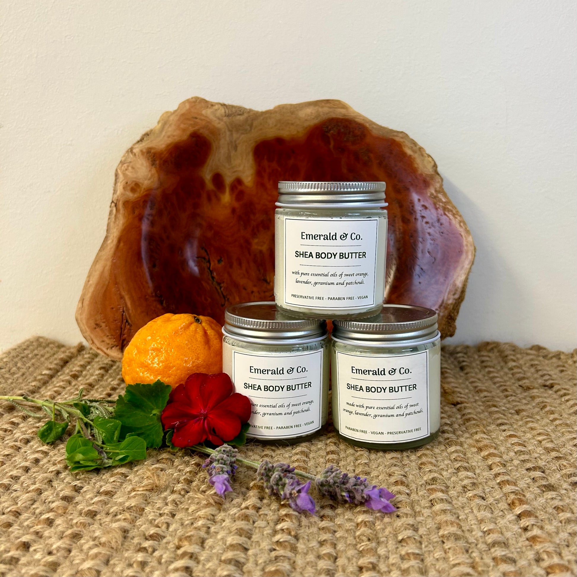 Three jars with silver lids, wooden plate behind them and some flowers and a mandarin beside them