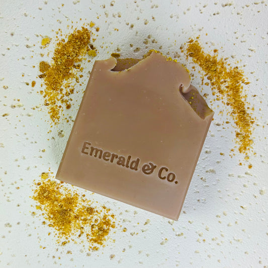 Bar of soap with 'Emerald & Co.' branding on a textured surface with gold powder.